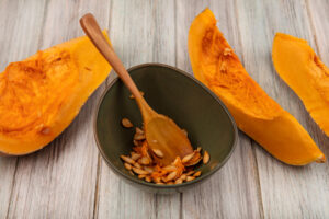 top-view-tasty-orange-pumpkin-slices-with-seeds-bowl-with-wooden-spoon-grey-wooden-surface